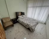 تخت خواب با روتختی سفید و مبل قهوه ای رنگ اتاق خواب آپارتمان در خمینی شهر