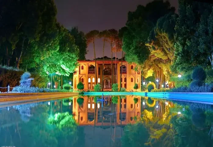 منعکس شدن نمای ساختمان قدیمی کاخ هشت بهشت اصفهان بر روی استخر در کنار درختان سرسبز و بلند قامت در شب 1564156